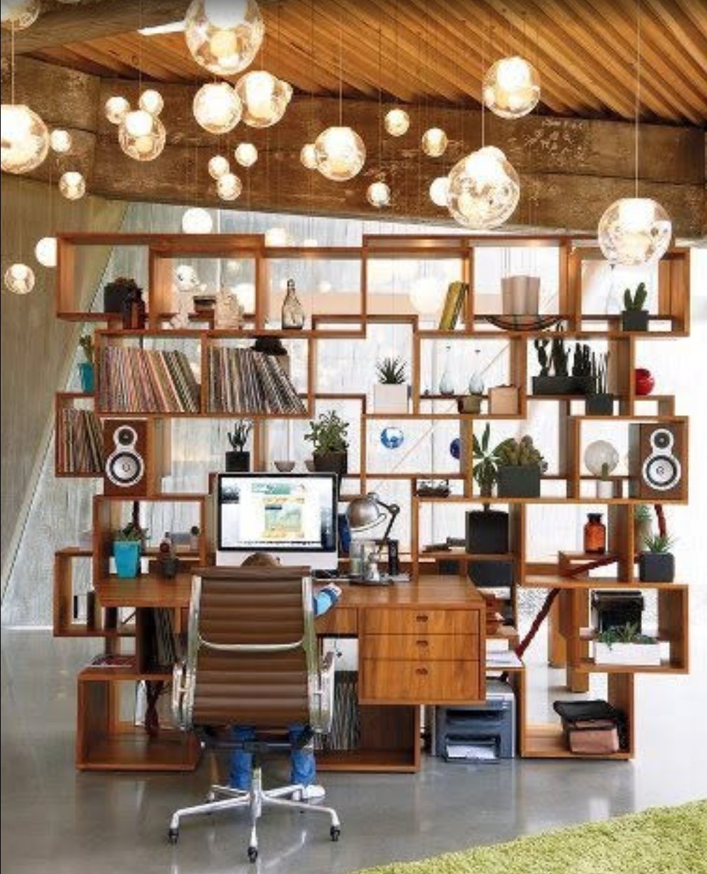 Loft-Arbeitsbereich mit skulpturalem Holz-Regalsystem und einem Cluster transparenter Pendelleuchten an der Holzbalkendecke.