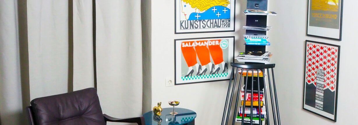 Wohnecke mit Lederfauteuil, Vintage-Beistelltisch und einer Sammlung gerahmter Kunstplakate.